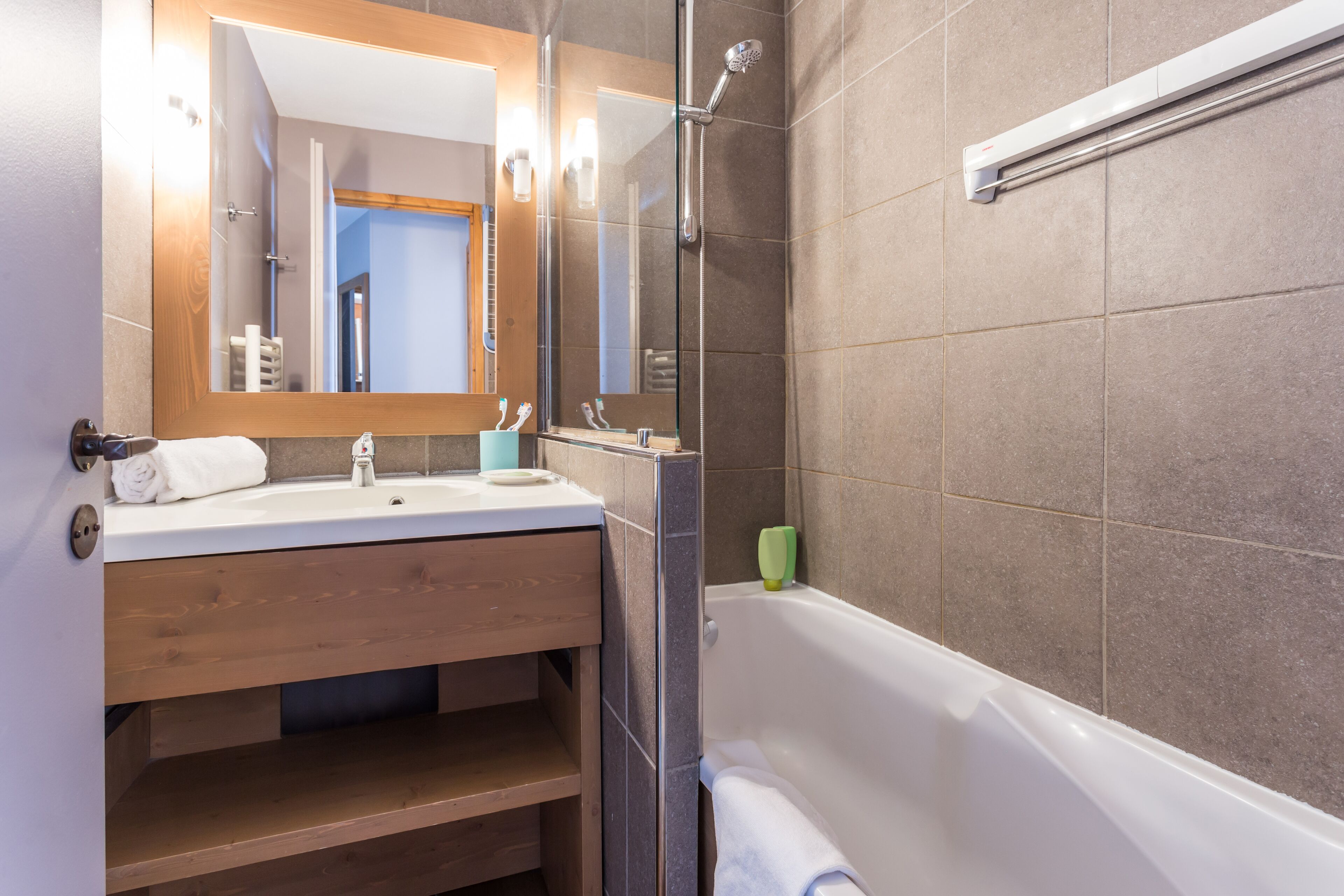 A modern bathroom with a wooden vanity, a large mirror, a shower with a glass door, and a bathtub.