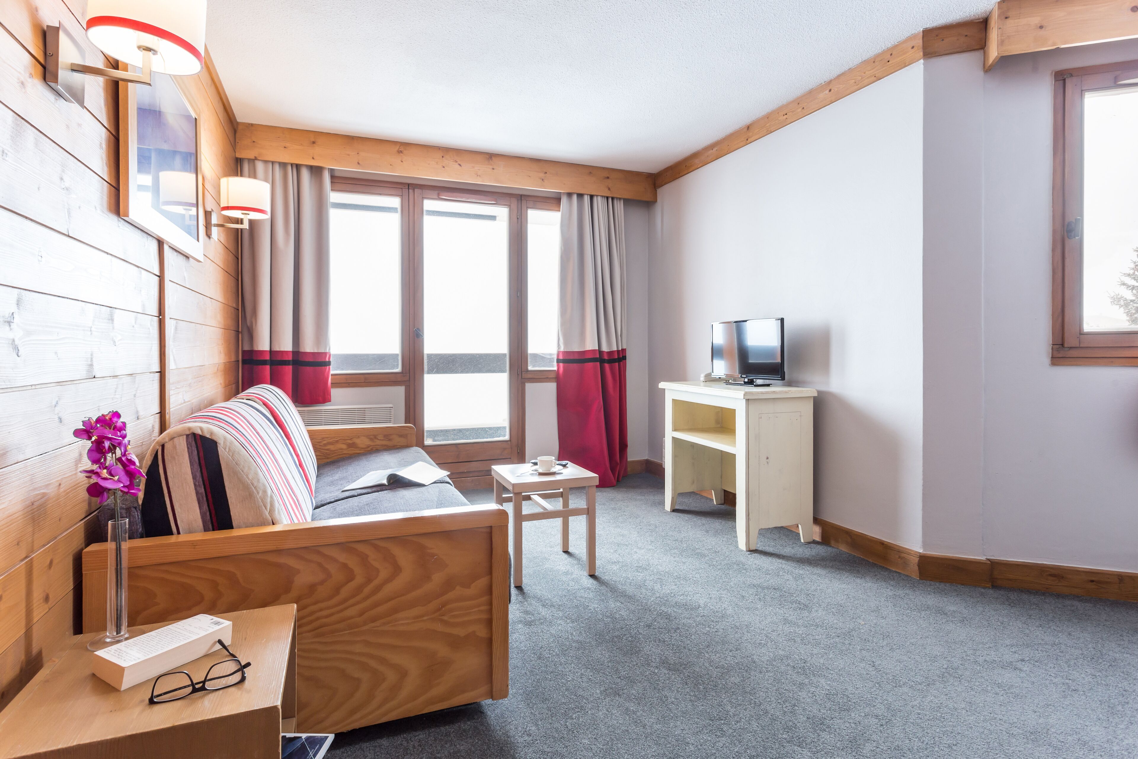 A cozy room with a wooden bed, a small table with a TV, and a window with curtains.
