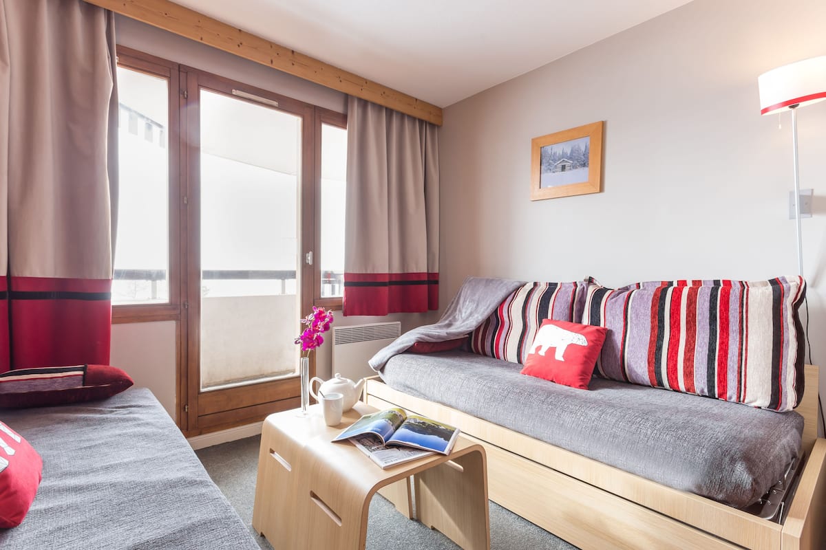A modern room with a sofa, a small table with a book and a vase, and a window with curtains.