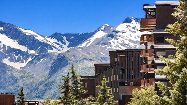 A modern building with a wooden facade, a balcony, and a view of snow-capped mountains. - Pierre & Vacances Residence L'Ours Blanc (Huez)