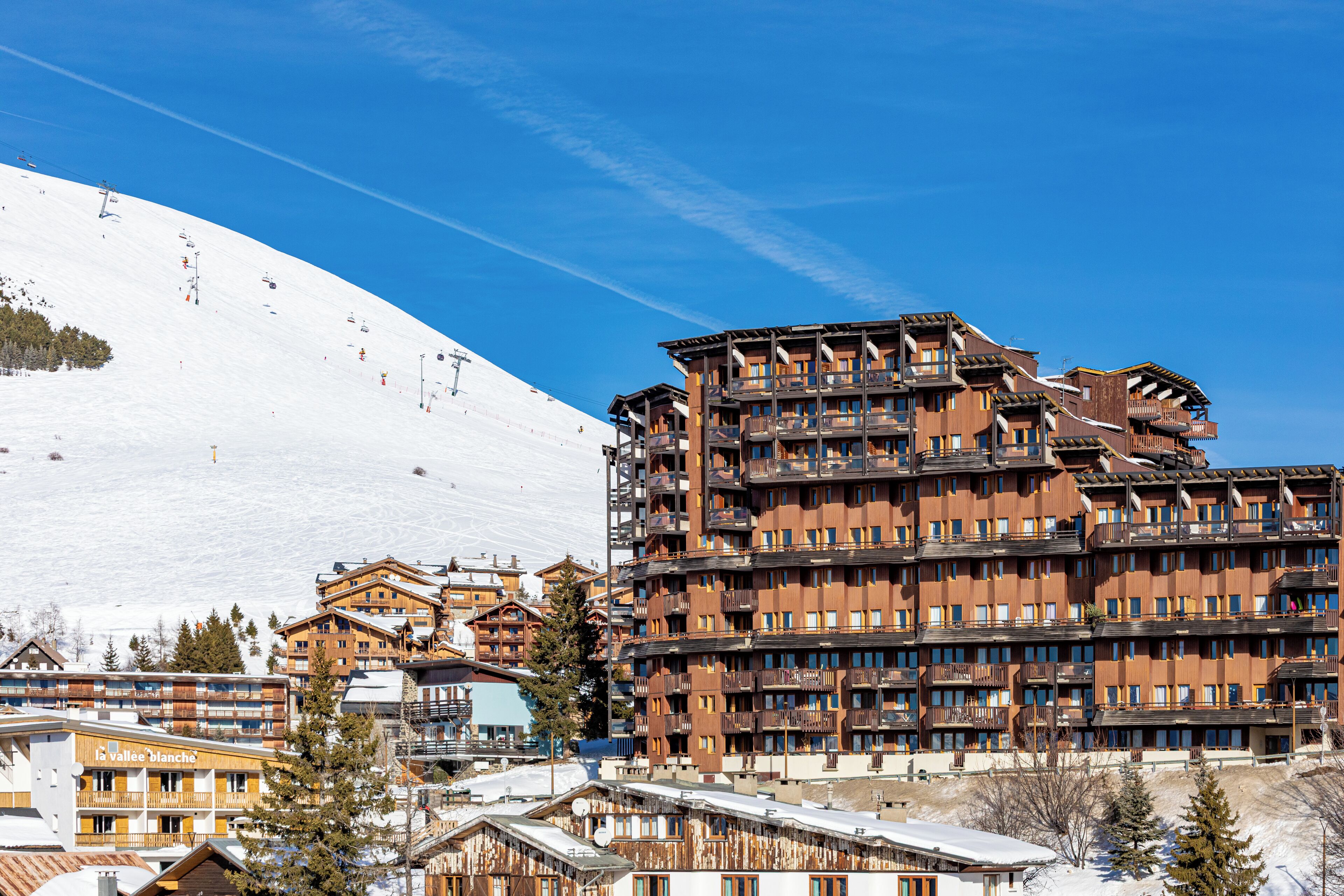 A multi-story hotel with balconies, ski lift tracks, and snow-covered surroundings.