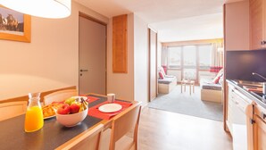 A modern kitchen with a dining area, a large window, and a view of the living room. - Pierre & Vacances Residence L'Ours Blanc (Huez)