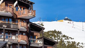 A multi-story wooden building with balconies, a ski slope in the background, and a clear blue sky. - Pierre & Vacances Residence L'Ours Blanc (Huez)