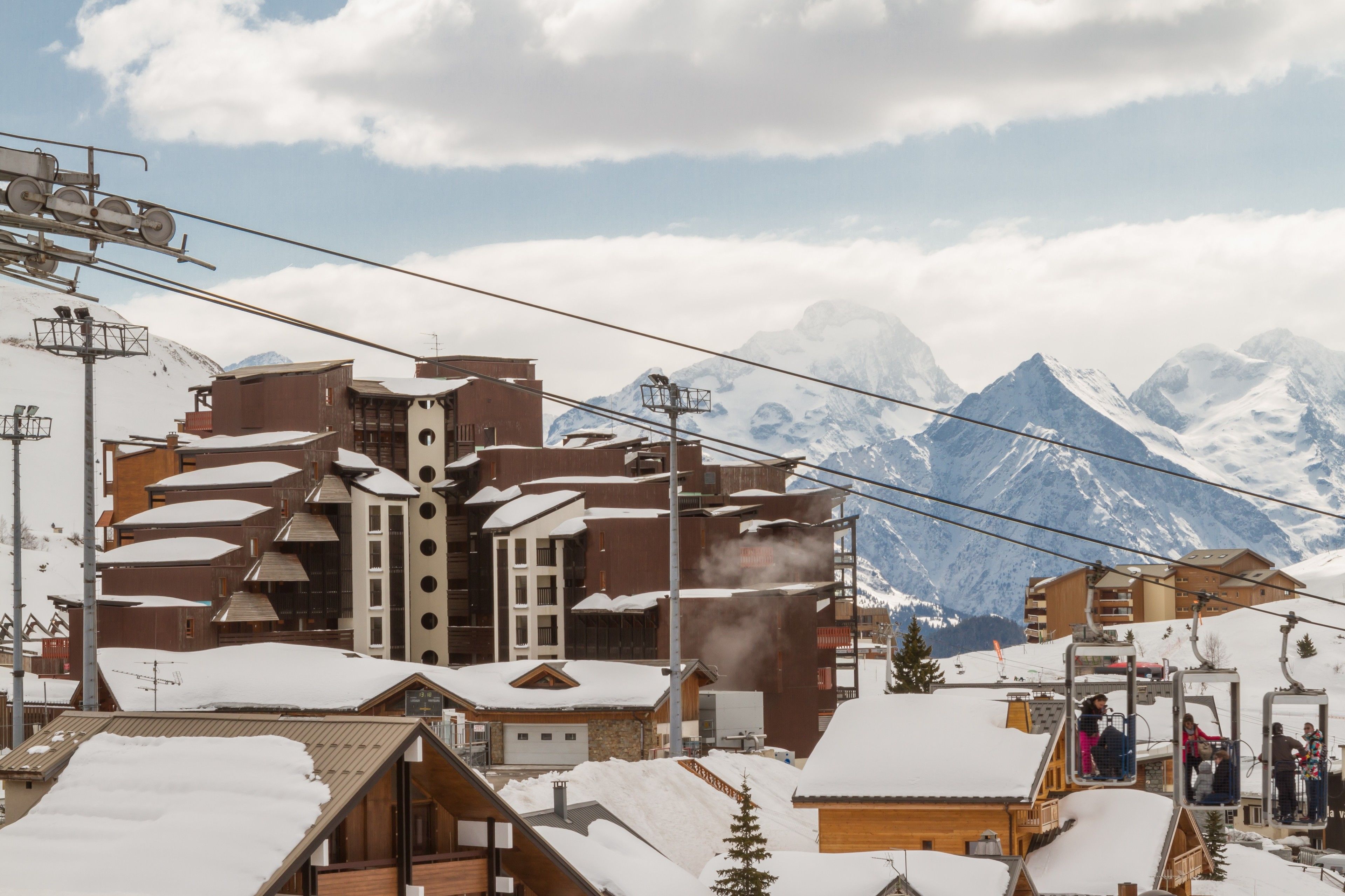 A ski resort with wooden buildings, a ski lift, and snow-covered mountains in the background.