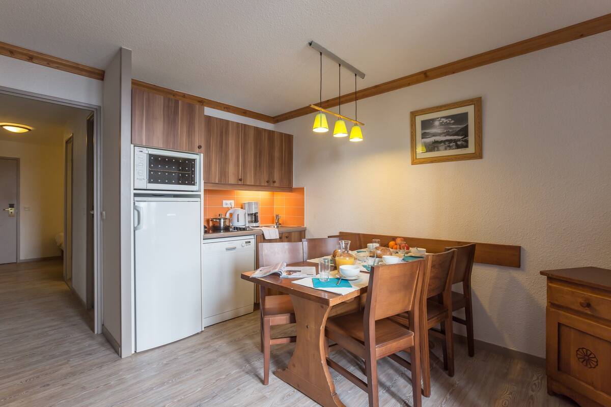 A compact kitchen with wooden cabinets, a built-in oven, and a dining area with a table and chairs.