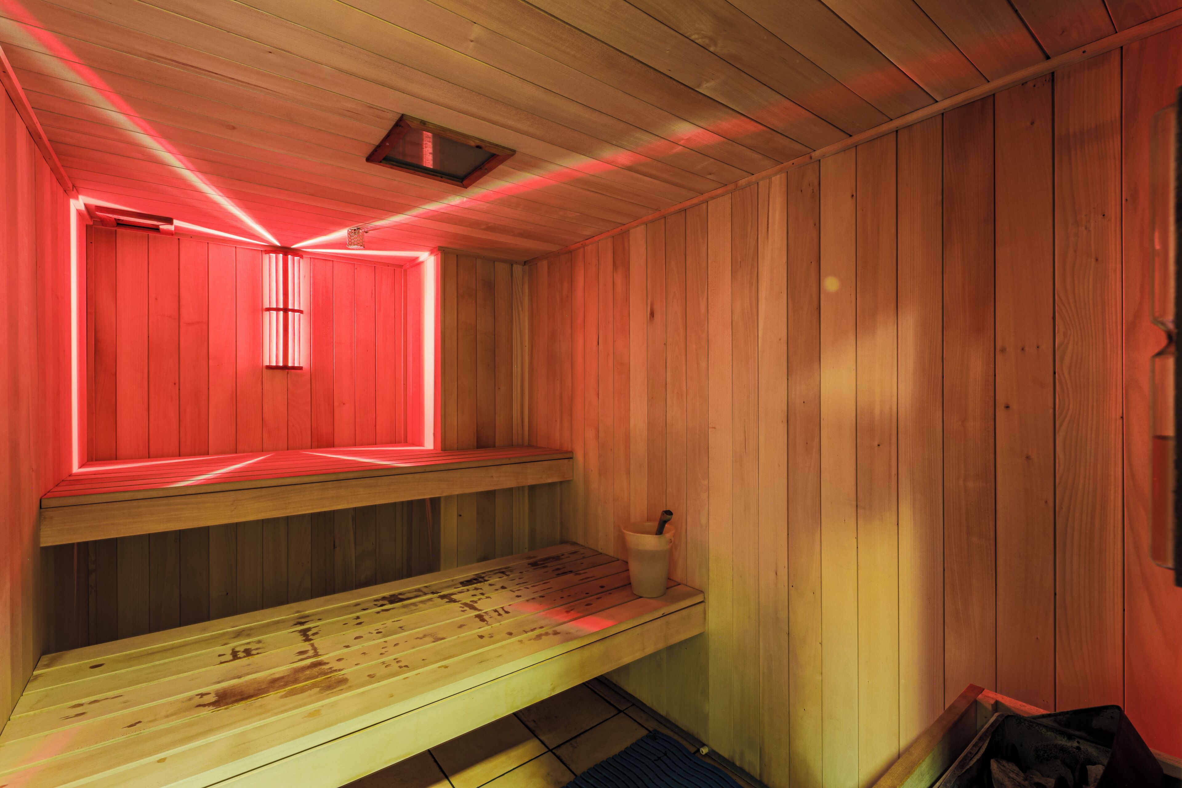 A sauna room with wooden benches and a red-lit ceiling.