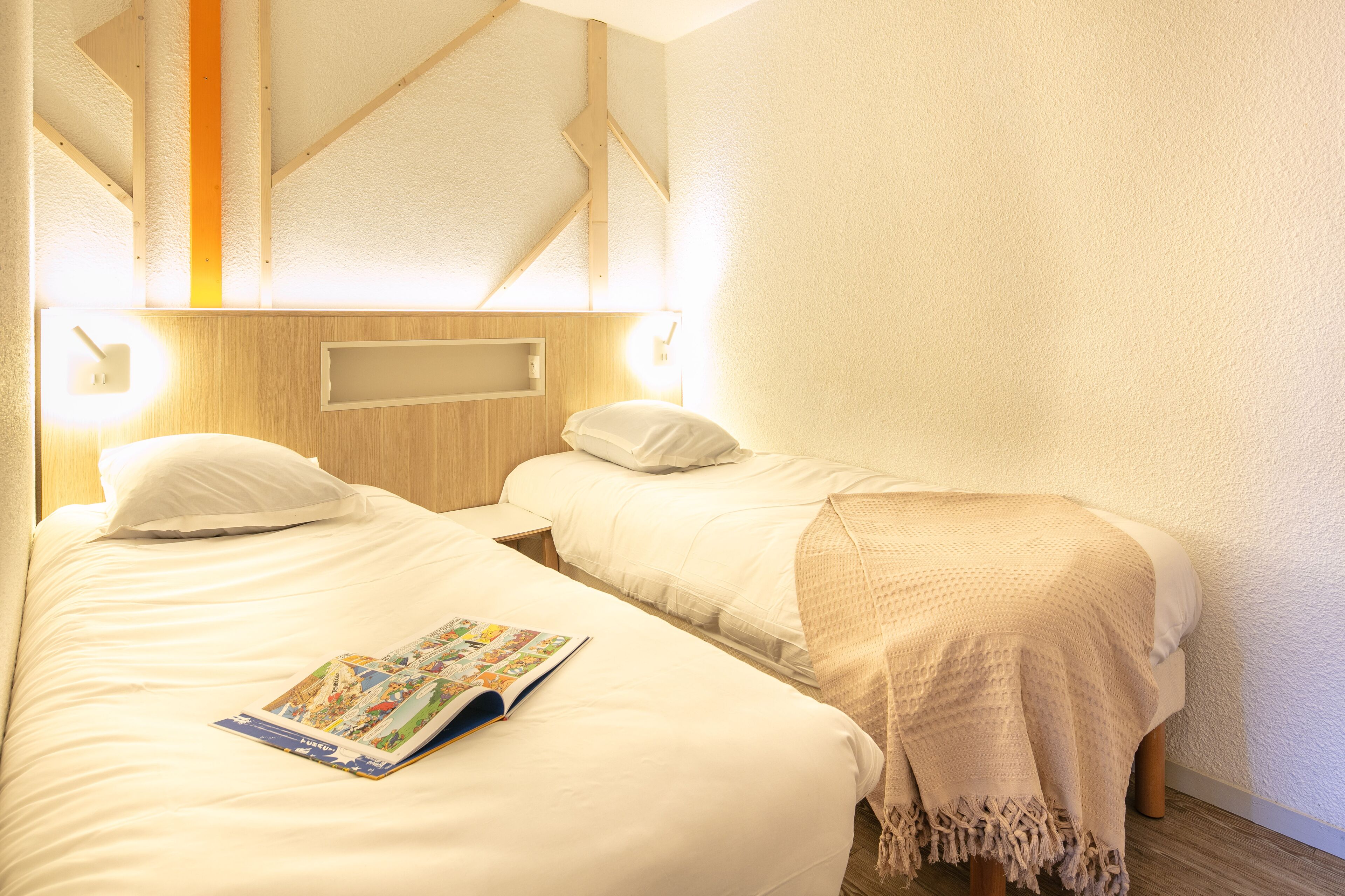 A hotel room with two beds, a wooden headboard, and a magazine on the left bed.