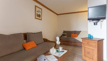 A furnished room with a sofa, a wooden nightstand, a table with a book and a vase, and a bed with pillows.