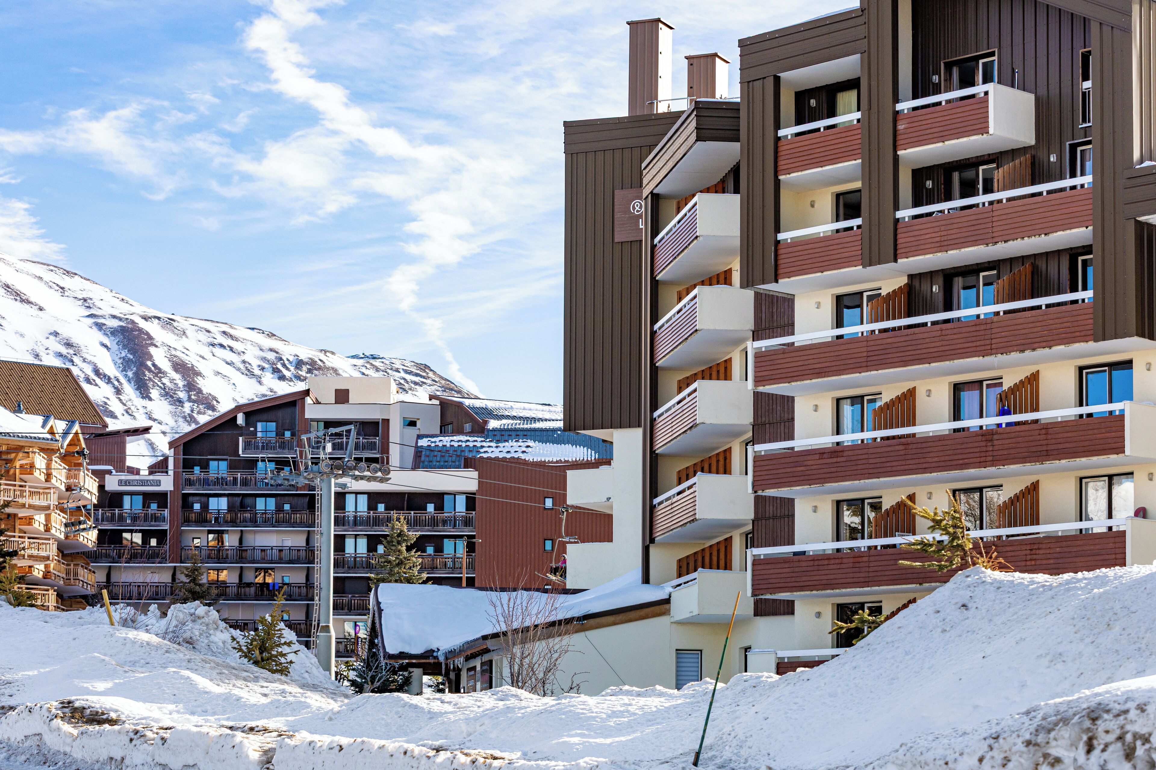 A multi-story hotel with balconies, a ski slope in the background, and snow on the ground.