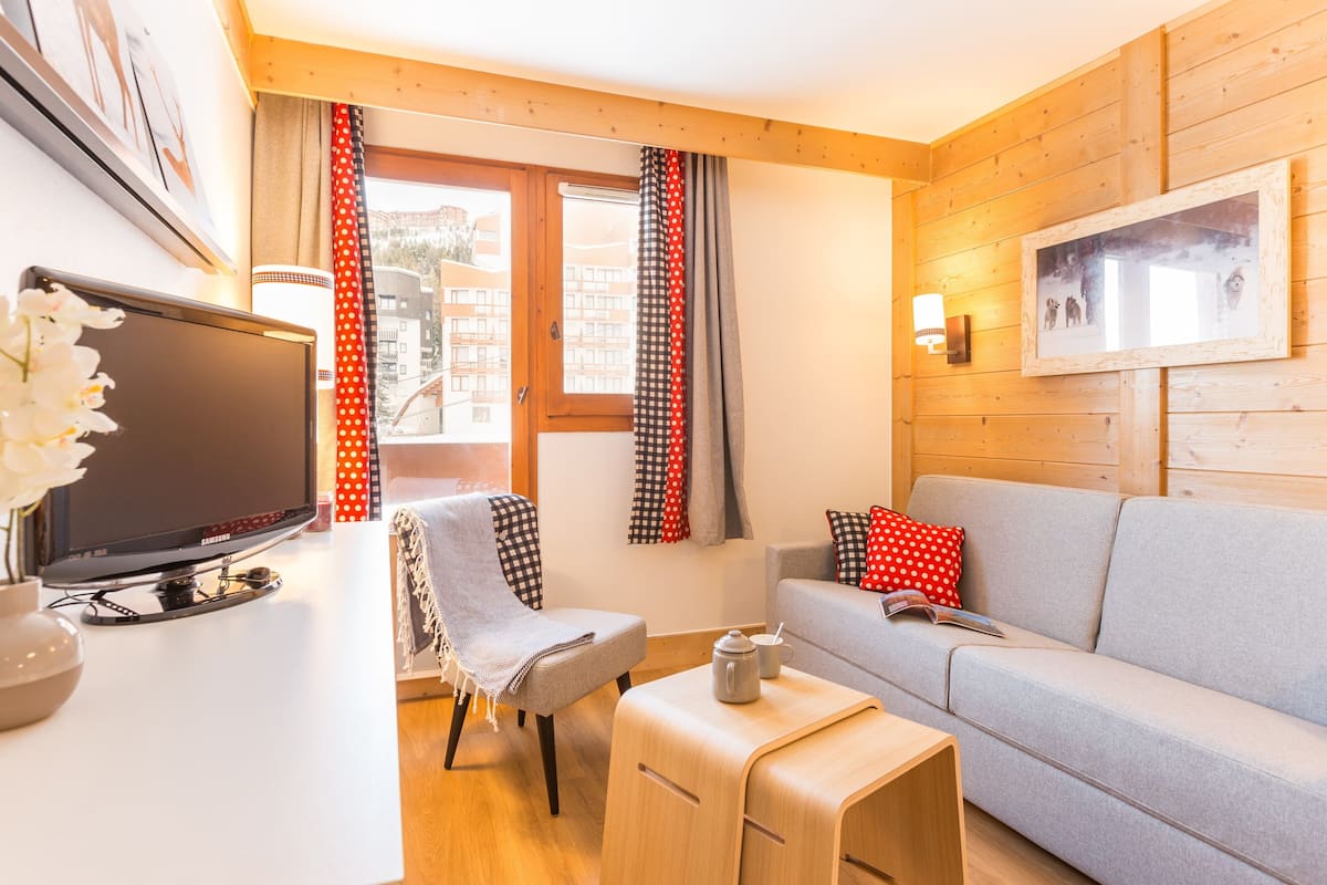 Una sala de estar moderna con un sofá, una mesita, un televisor y una ventana con cortinas.