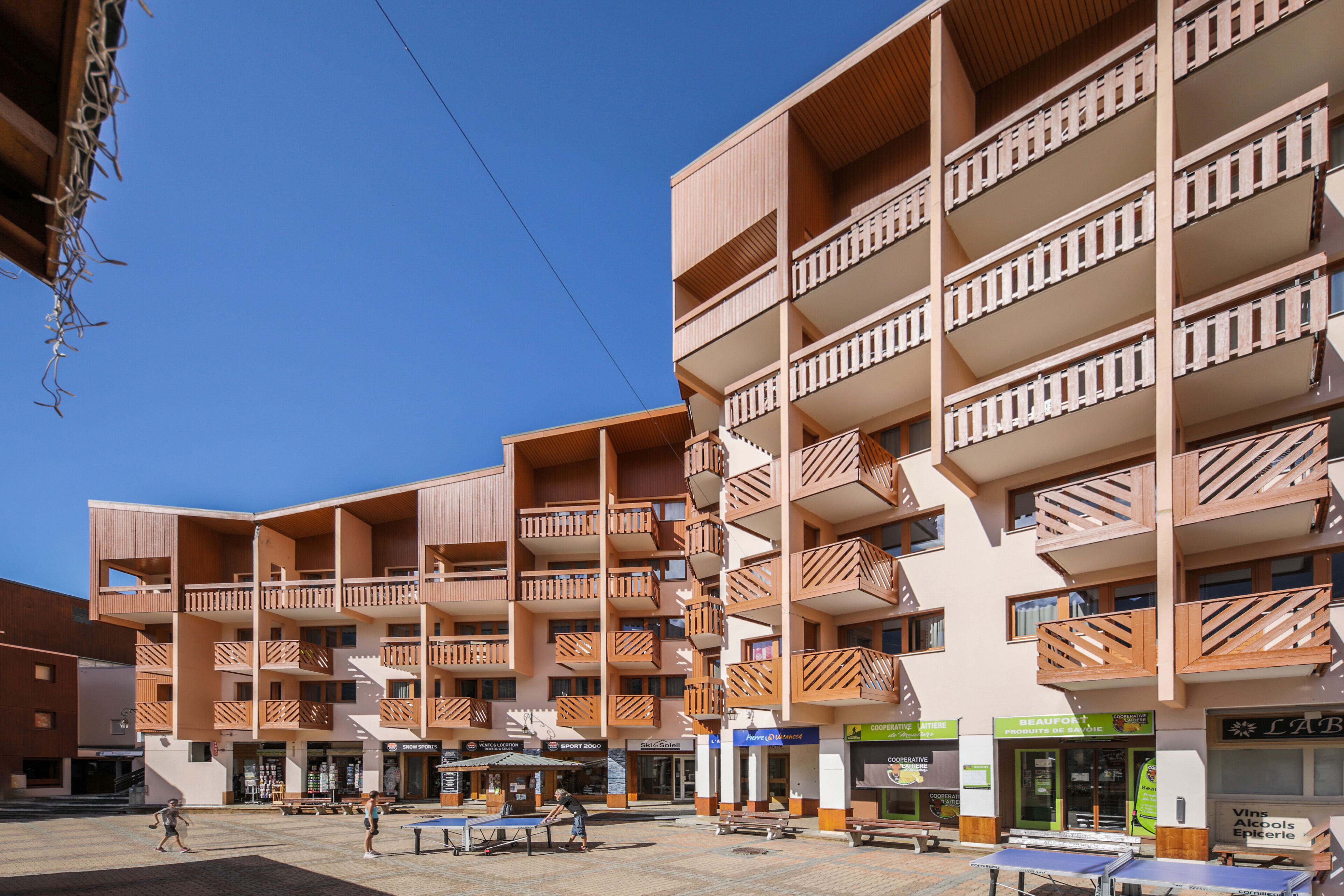 A multi-story building with balconies, outdoor seating, and shops on the ground floor.