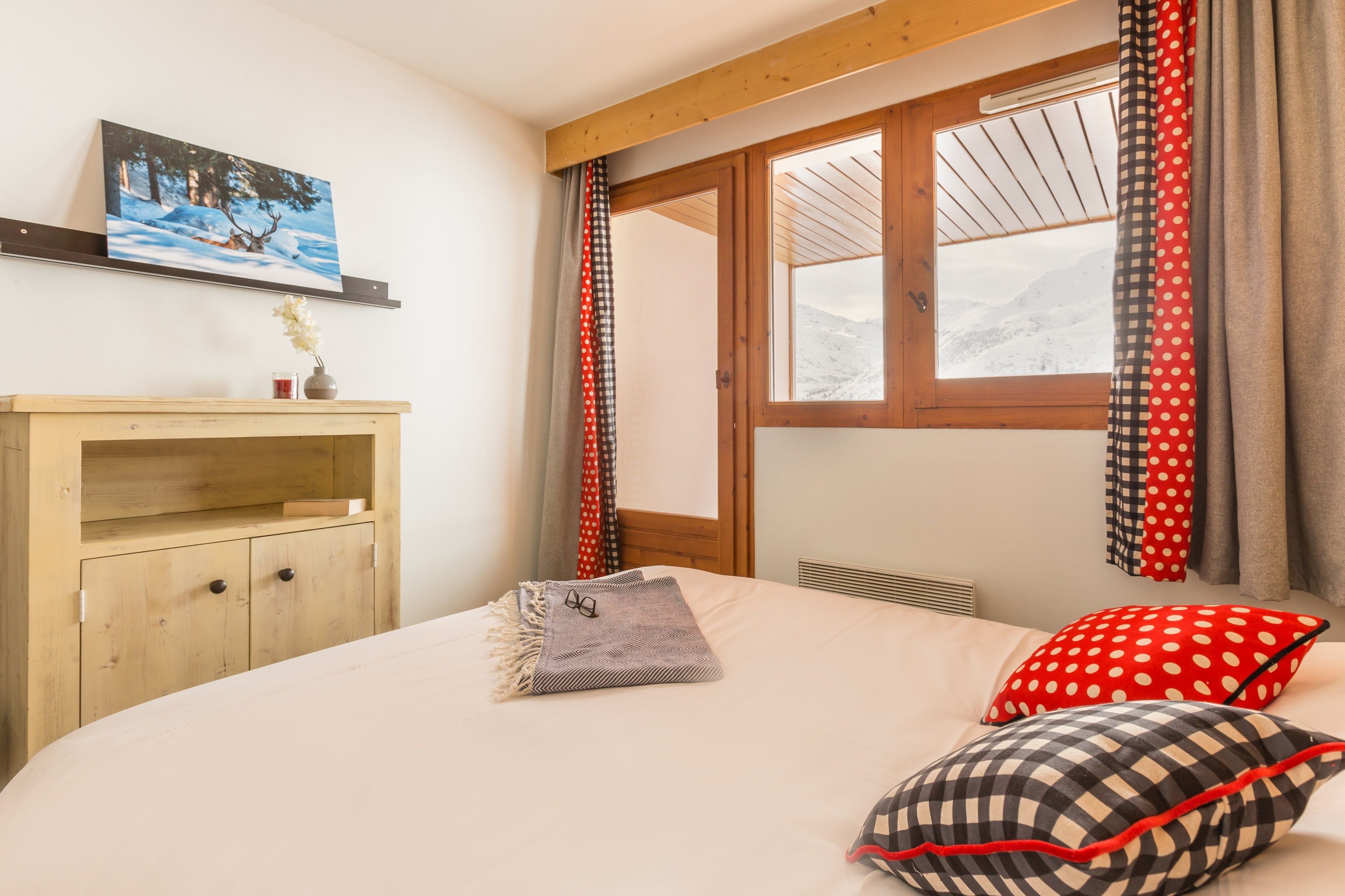 A bedroom with a bed, a wooden dresser, a window with curtains, and a painting on the wall.