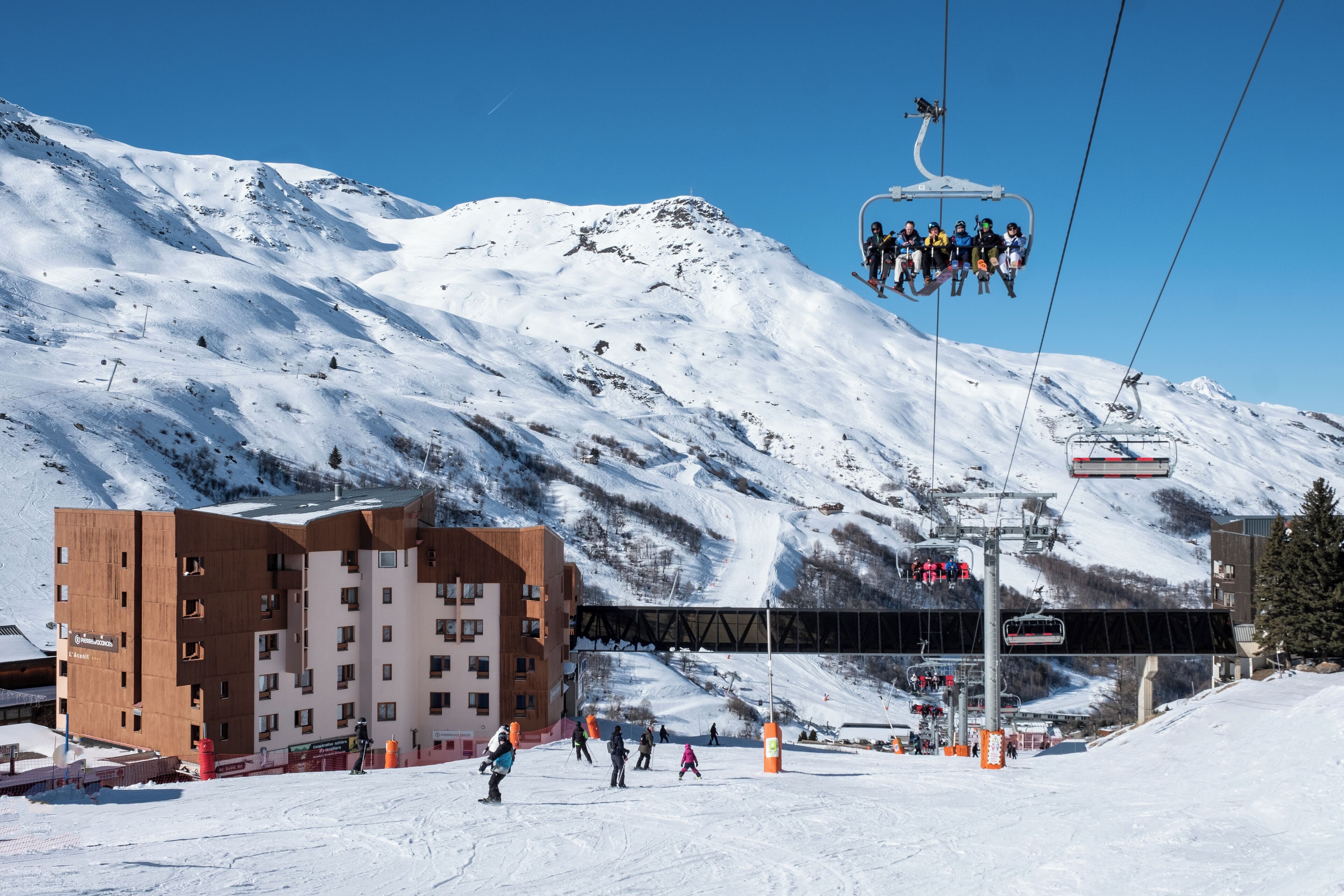 A ski resort with a lift system, a building with multiple floors, and a snowy mountain backdrop.
