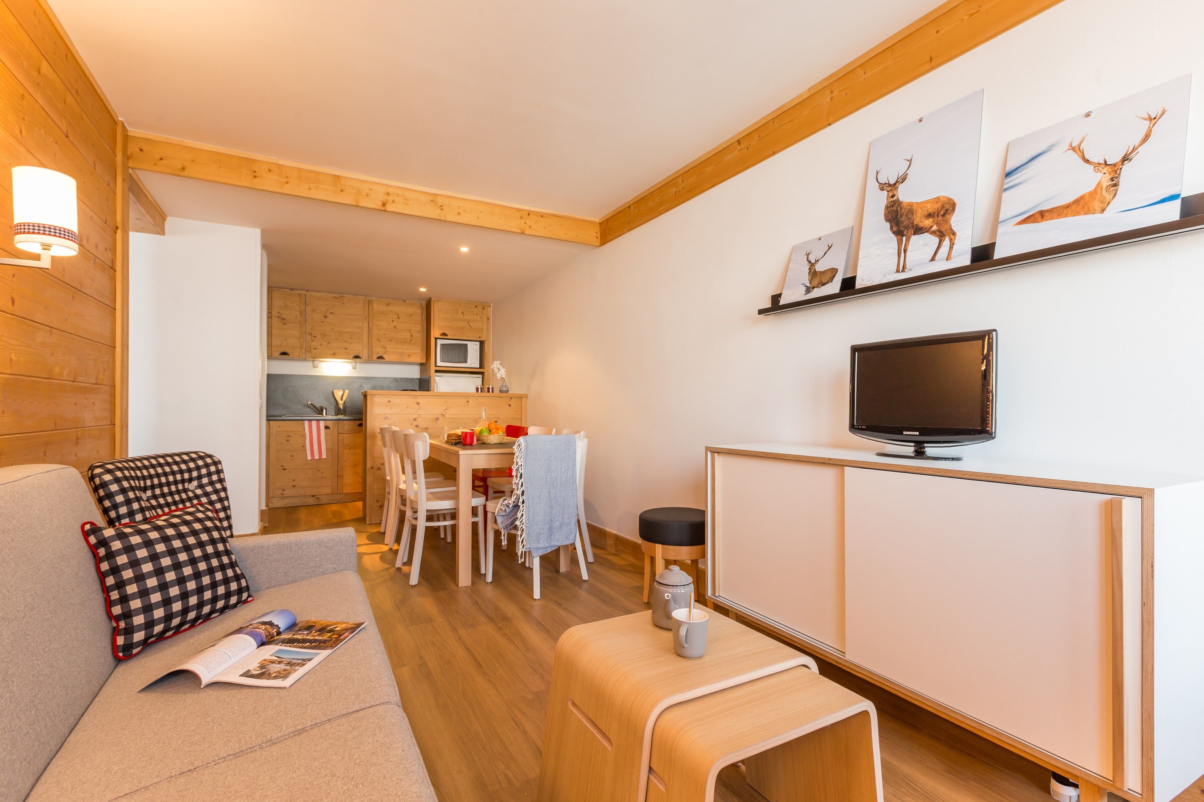 A cozy living room with a sofa, a coffee table, a TV, and a kitchen in the background.