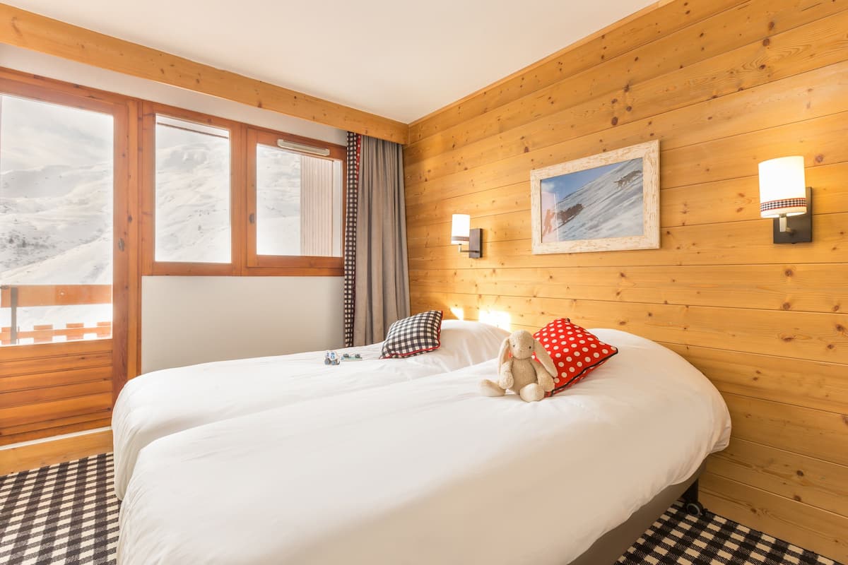 Habitación de hotel con interior de madera, una cama grande con ropa blanca, vista a un paisaje nevado por la ventana y un cuadro enmarcado en la pared.