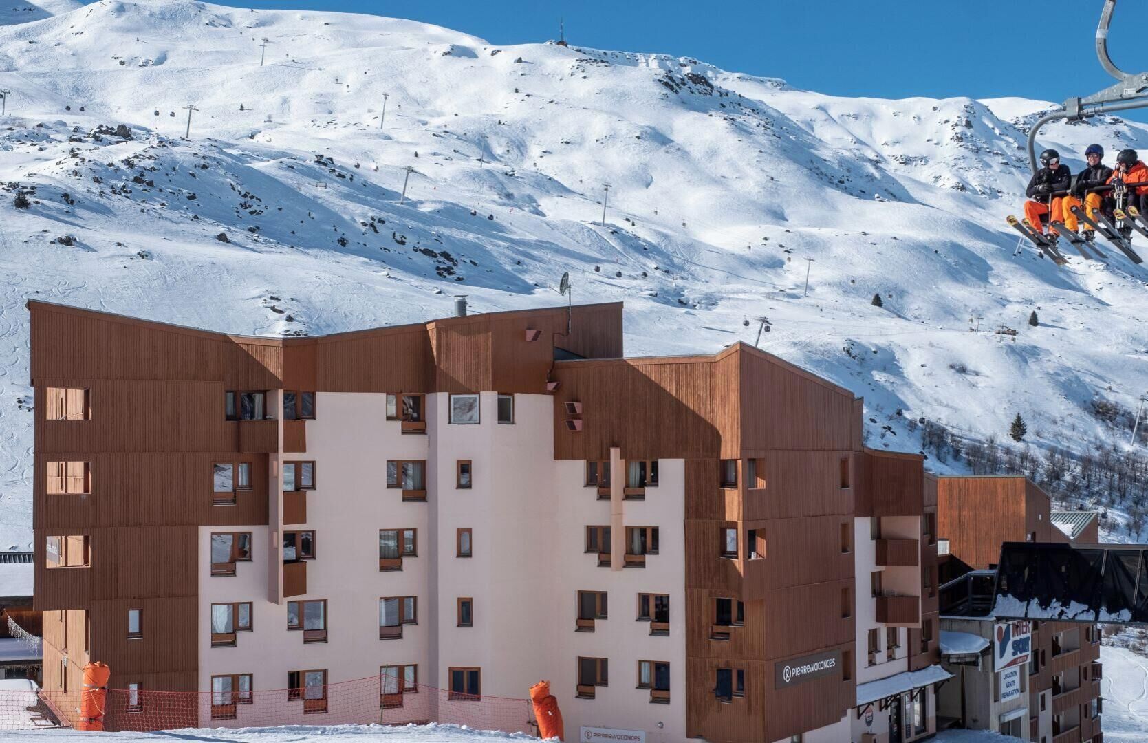 Ein modernes Hotel mit mehreren Etagen, Sesselliften und einem verschneiten Bergpanorama.