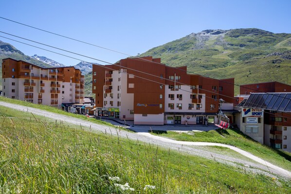 A multi-story hotel with a ski lift in the background, surrounded by green hills and mountains.