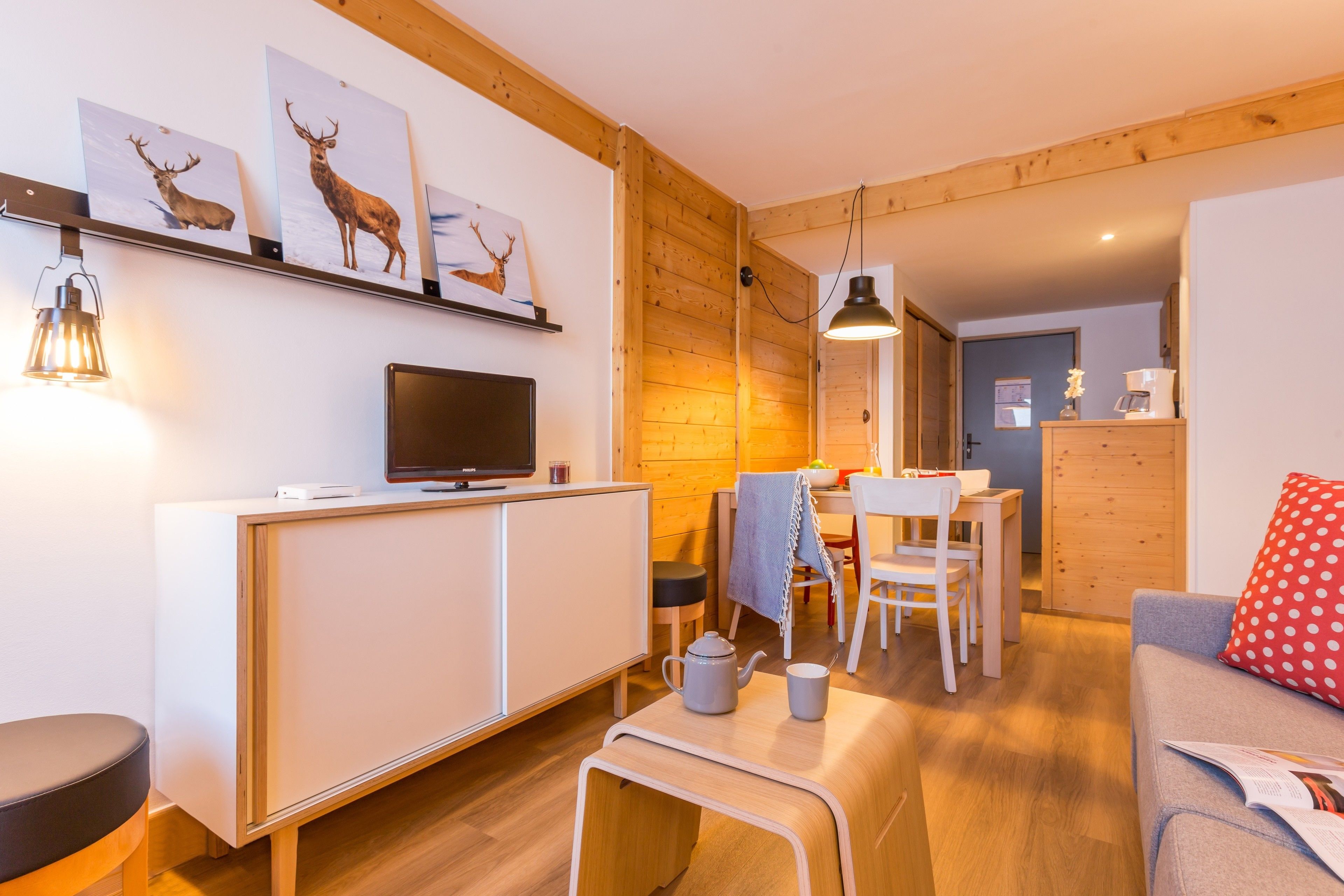 A modern living room with a wooden floor, white furniture, a television, and artwork on the wall.
