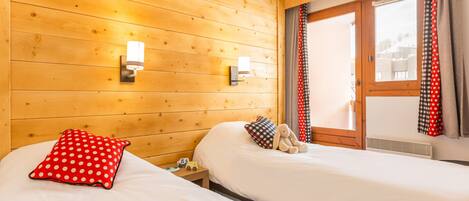 A hotel room with wooden panel walls, two beds with white bedding, a red polka dot pillow, a stuffed toy, and a window with curtains.