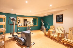 Un gimnasio con equipo de ejercicio, un espejo y sillas de madera.