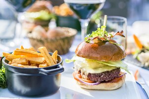 A meal consisting of a burger, fries, and a drink, with a glass of water and a bowl of salad in the background.