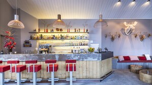 Zona de bar con taburetes de madera, estantes con botellas y elementos decorativos como una cabeza de alce y ramas.