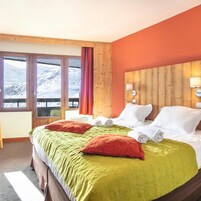 A hotel room with a bed, pillows, a window with a view of mountains, and a wooden headboard.