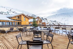 A wooden deck with outdoor seating, overlooking a snowy mountain.