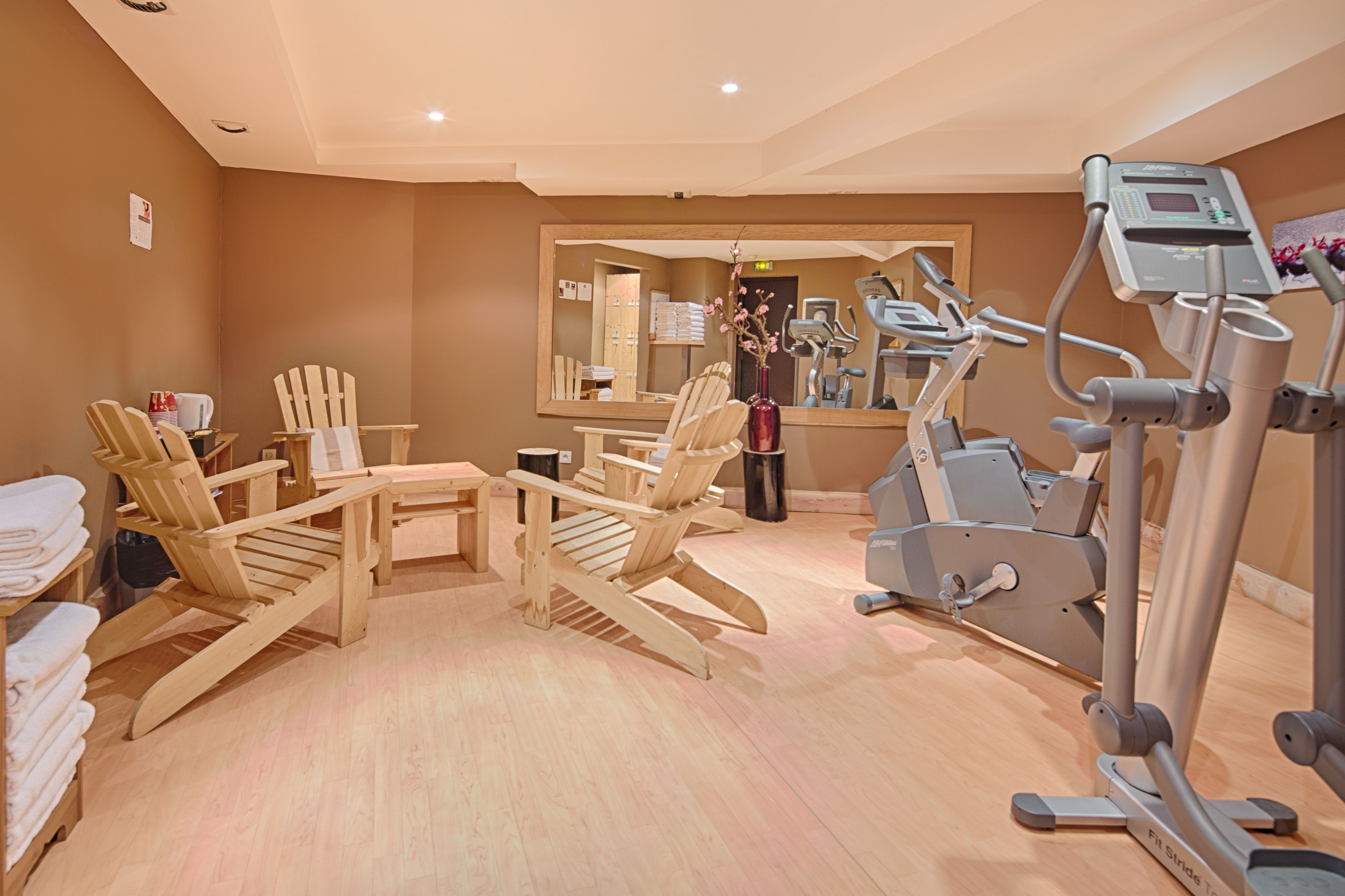 Un gimnasio con equipo de ejercicio, sillas de madera y un espejo.
