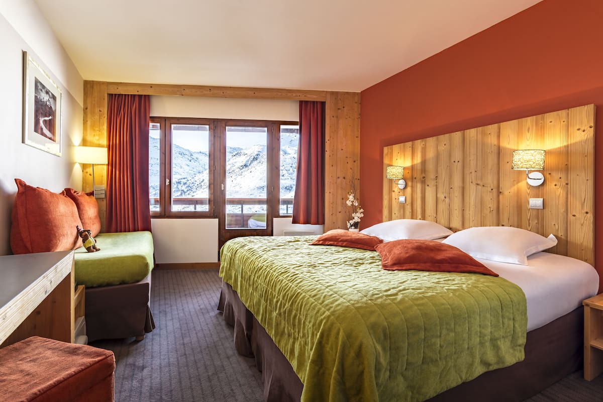 Quarto de hotel com cama, escrivaninha e janela com cortinas.