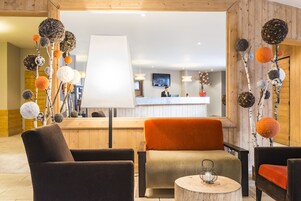 A hotel lobby with a reception desk, a large white lamp, and several chairs with orange and brown cushions.