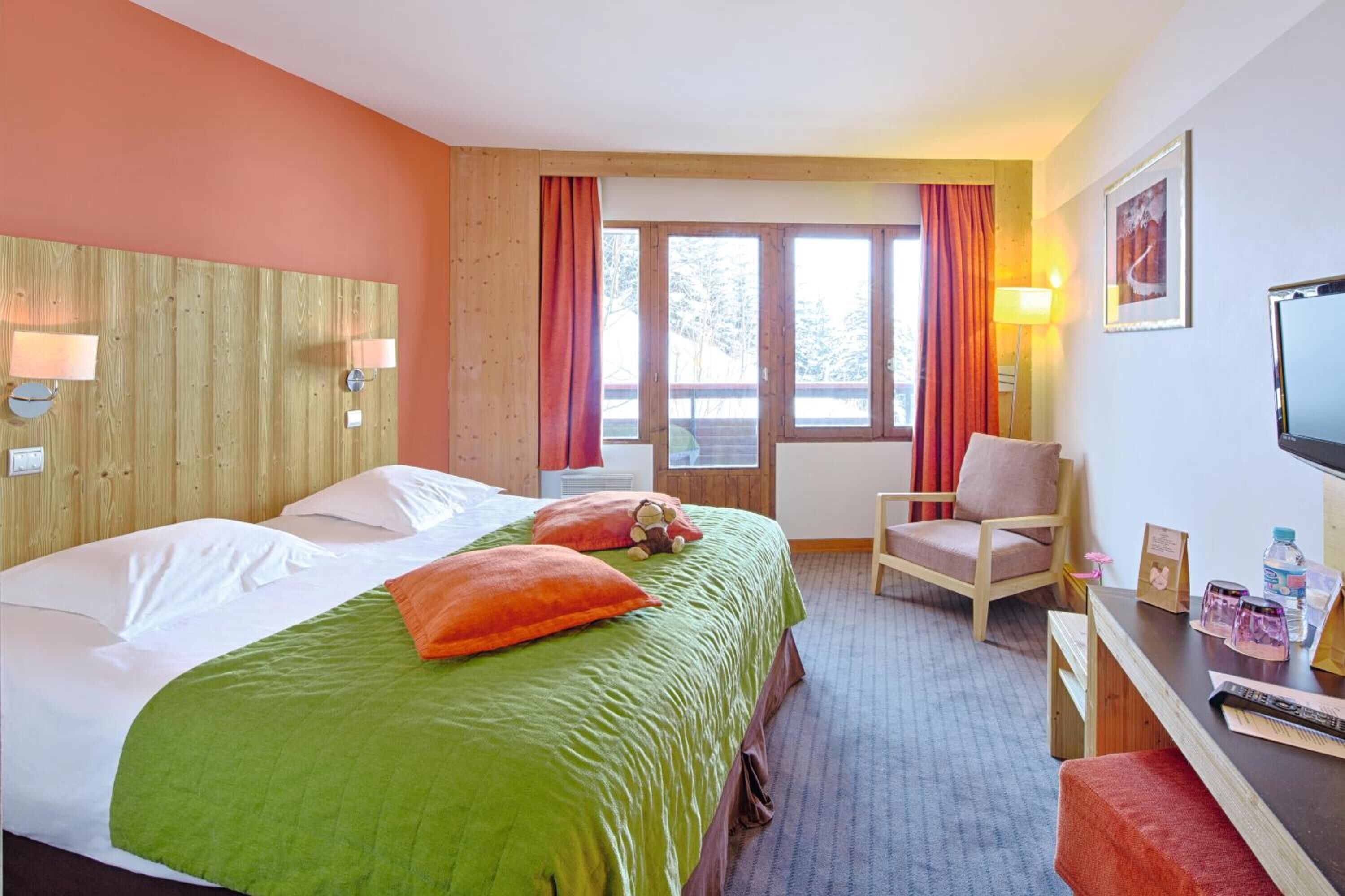 Habitación de hotel con cama, escritorio, silla, televisor y ventana con cortinas.