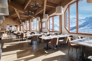 Une salle à manger spacieuse avec de hauts plafonds en bois, de grandes fenêtres offrant une vue sur les montagnes et des lustres modernes.