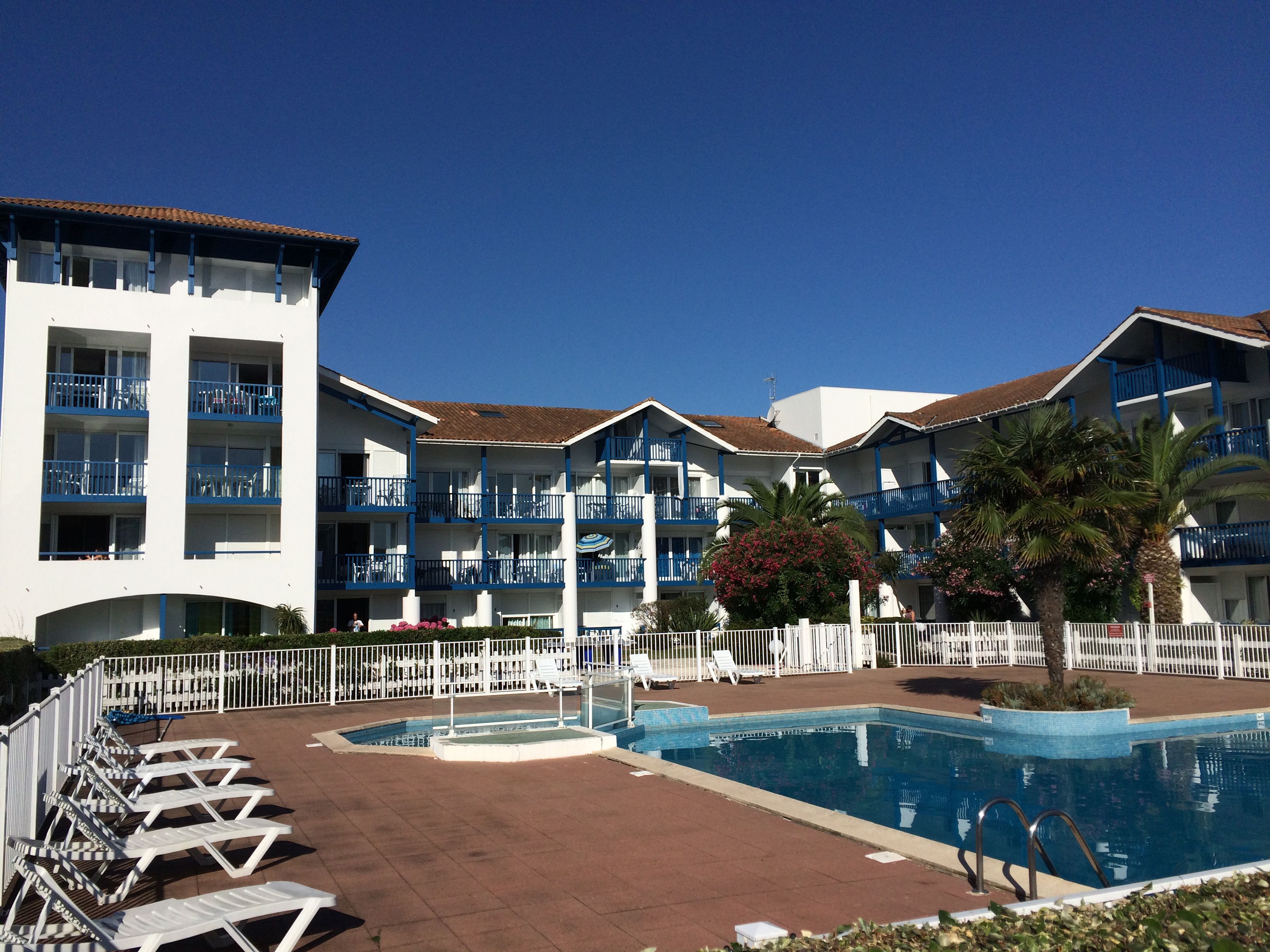 A hotel with multiple balconies, a swimming pool, and lounge chairs.