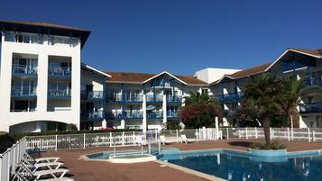 A hotel with multiple balconies, a swimming pool, and lounge chairs.