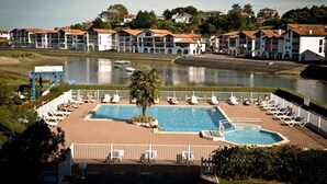 A swimming pool with lounge chairs and a view of a river and buildings in the background. - Résidence Fort Socoa (Urrugne)