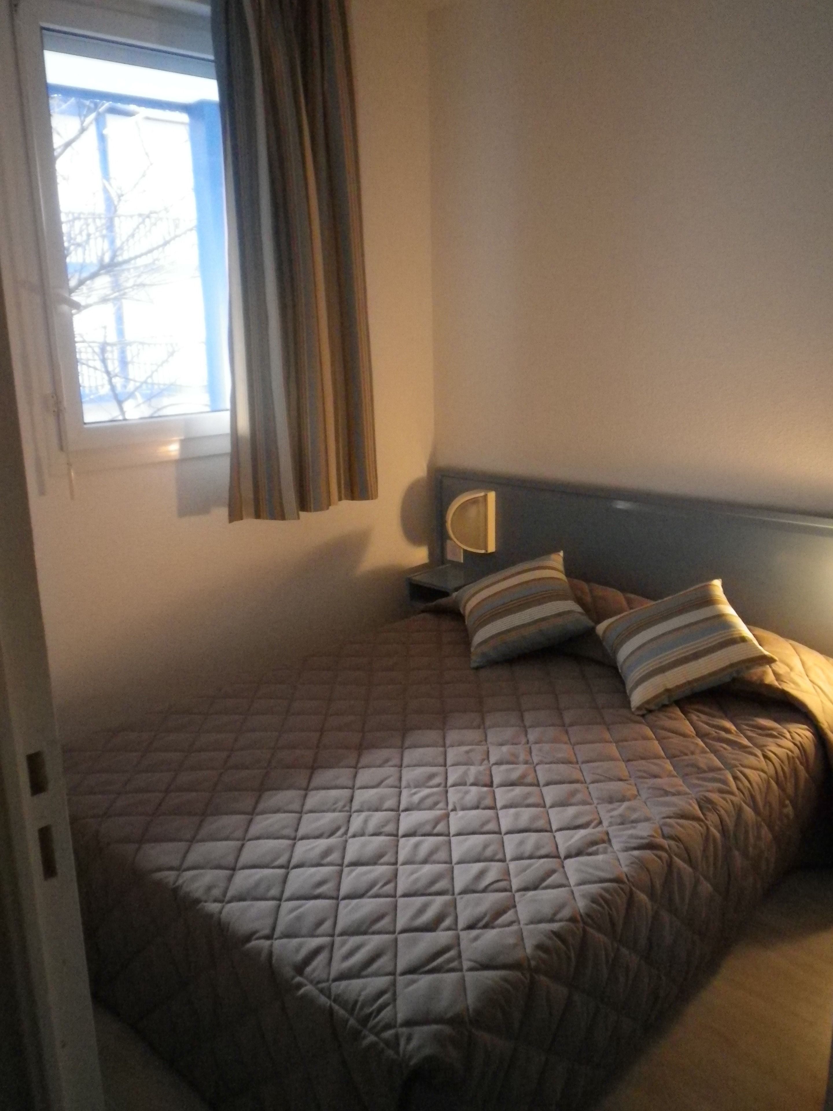 A bedroom with a bed, a nightstand, a lamp, and a window with curtains.