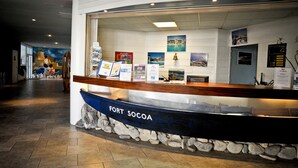 A reception desk labeled "FORT SOCOA" with informational brochures, a bell, and framed pictures on the wall. - Résidence Fort Socoa (Urrugne)