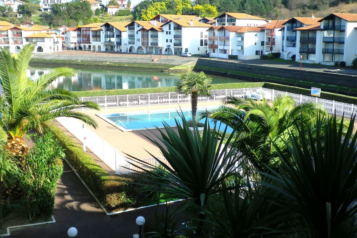 A hotel with multiple white buildings, a swimming pool, and a landscaped area with palm trees.