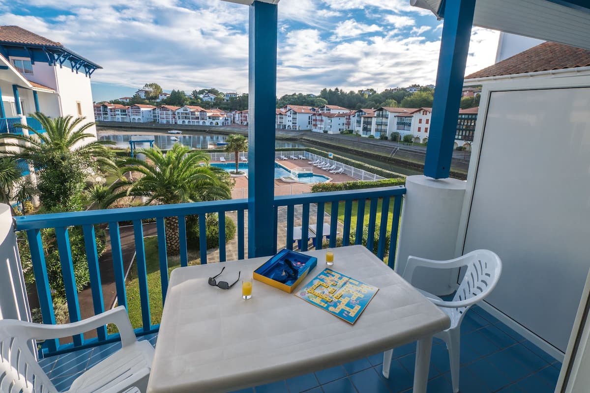 A balcony with a table, chairs, and a view of a swimming pool and buildings in the background.