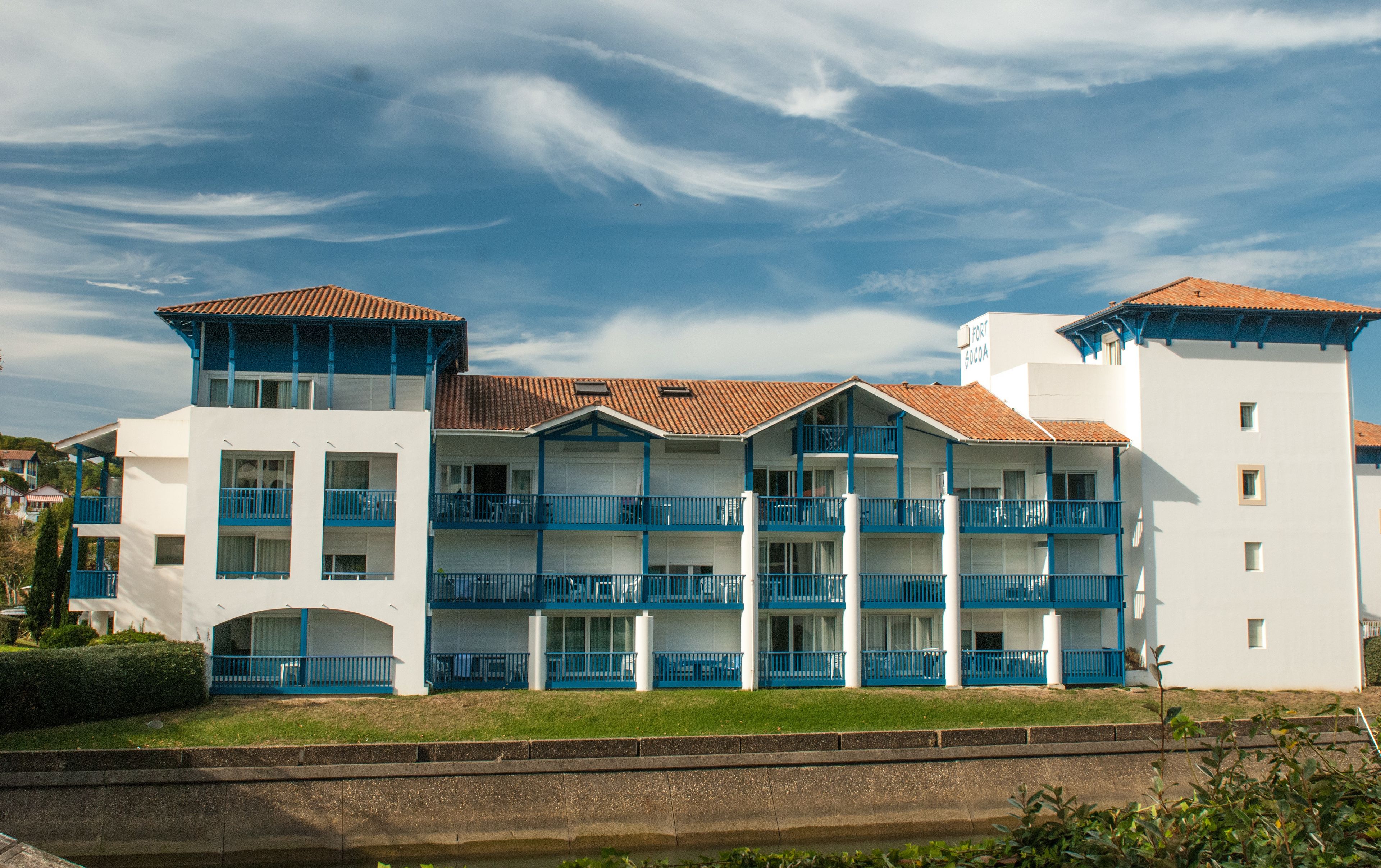 Un hotel de varios pisos con balcones, una piscina y cielo despejado.