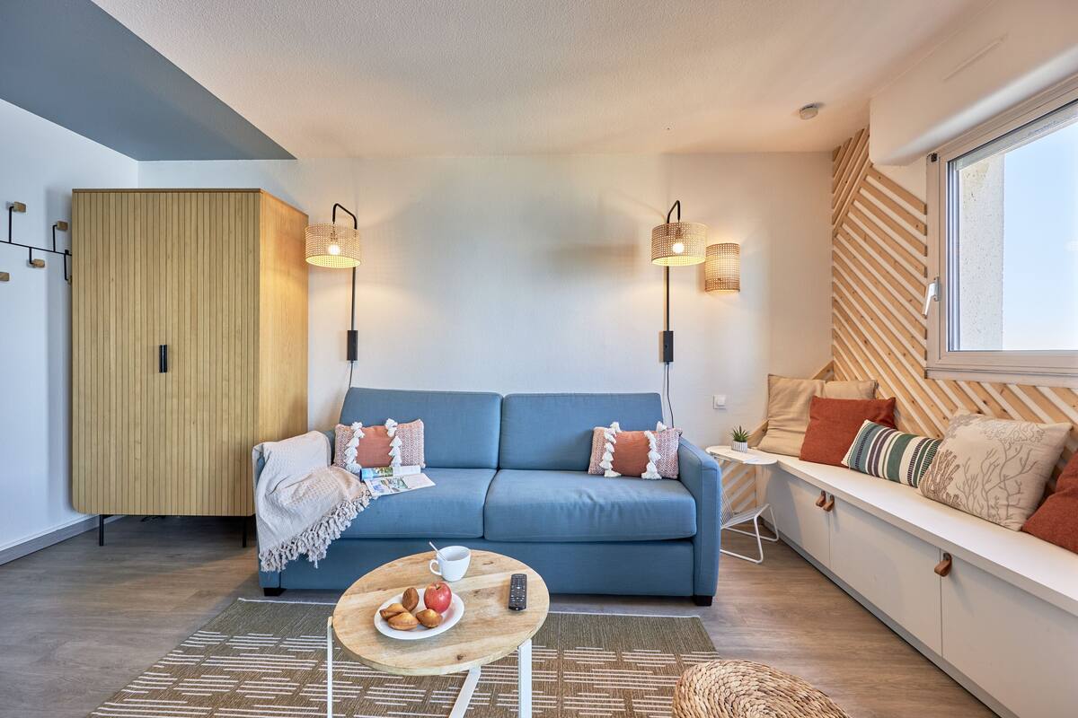 A modern living room with a blue sofa, wooden cabinet, and a white bench with cushions.