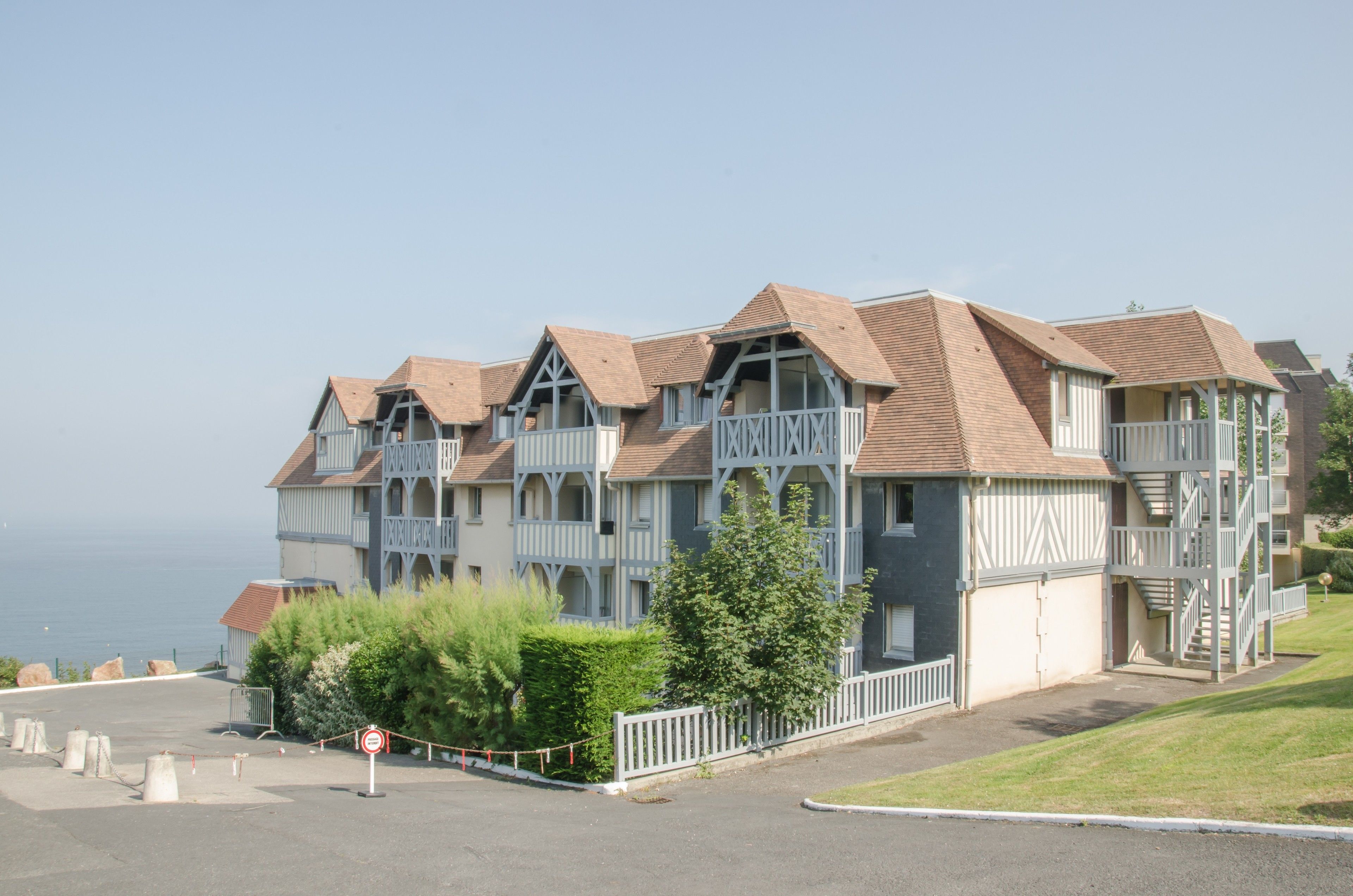A row of multi-story buildings with balconies, a clear sky, and a view of the sea.