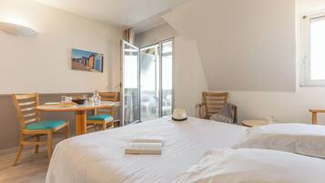 Une chambre d’hôtel avec un lit, une table à manger avec des chaises, une petite table avec une tasse, et un tableau accroché au mur.