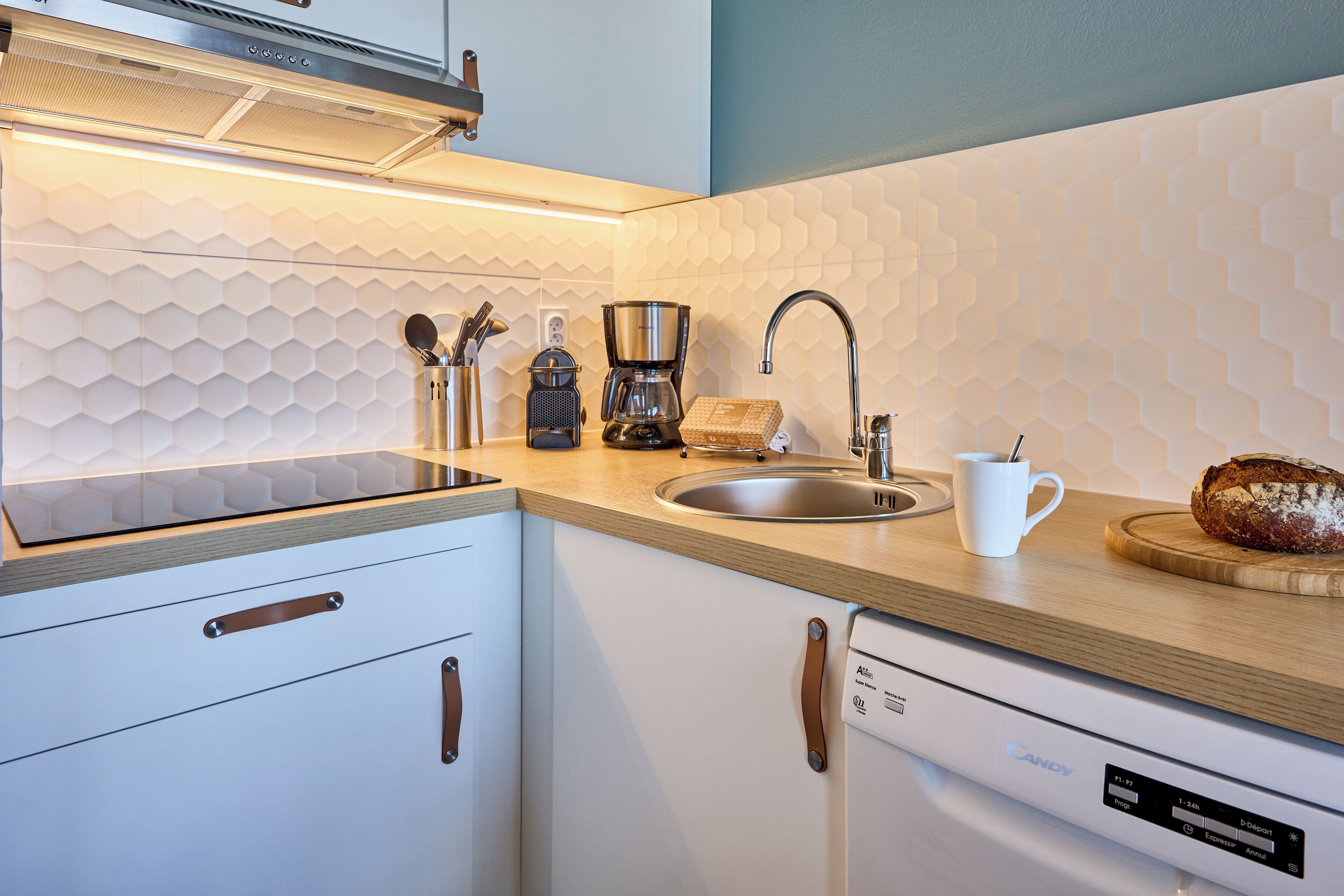 A modern kitchen with a stainless steel sink, a coffee maker, and a loaf of bread on the counter.
