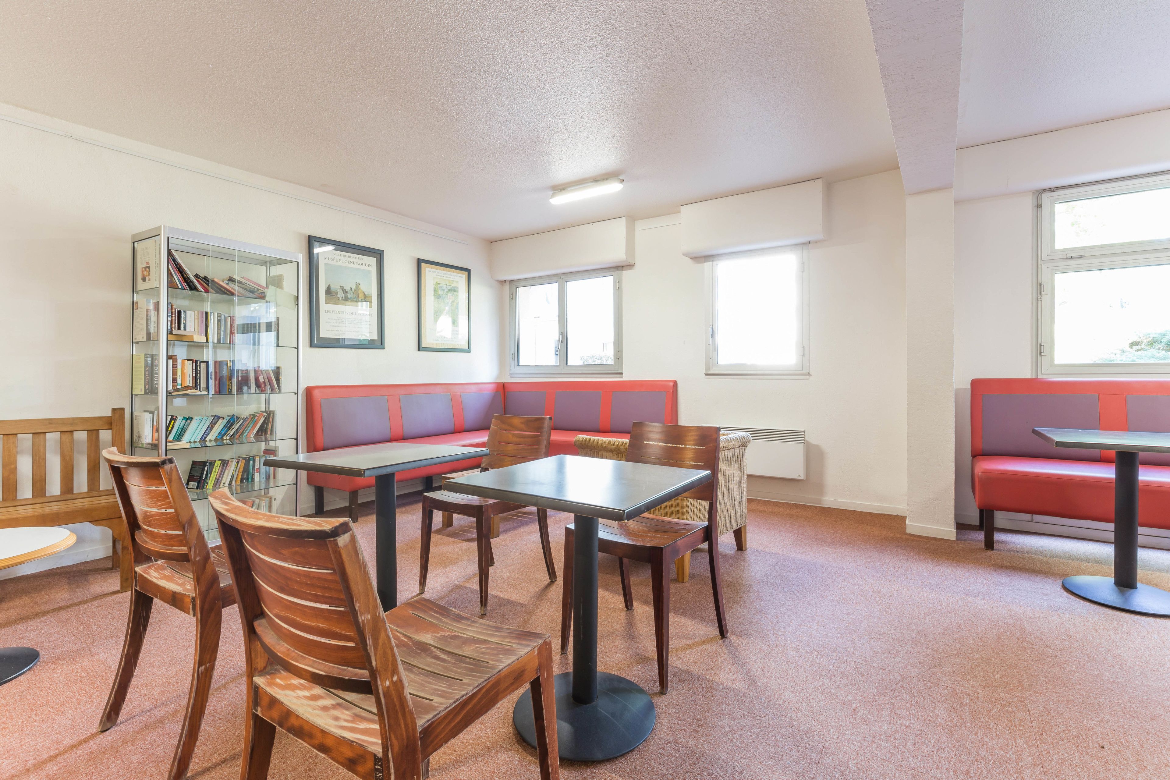 Et bibliotek med træstole, et bord, en rød bænk og en reol.