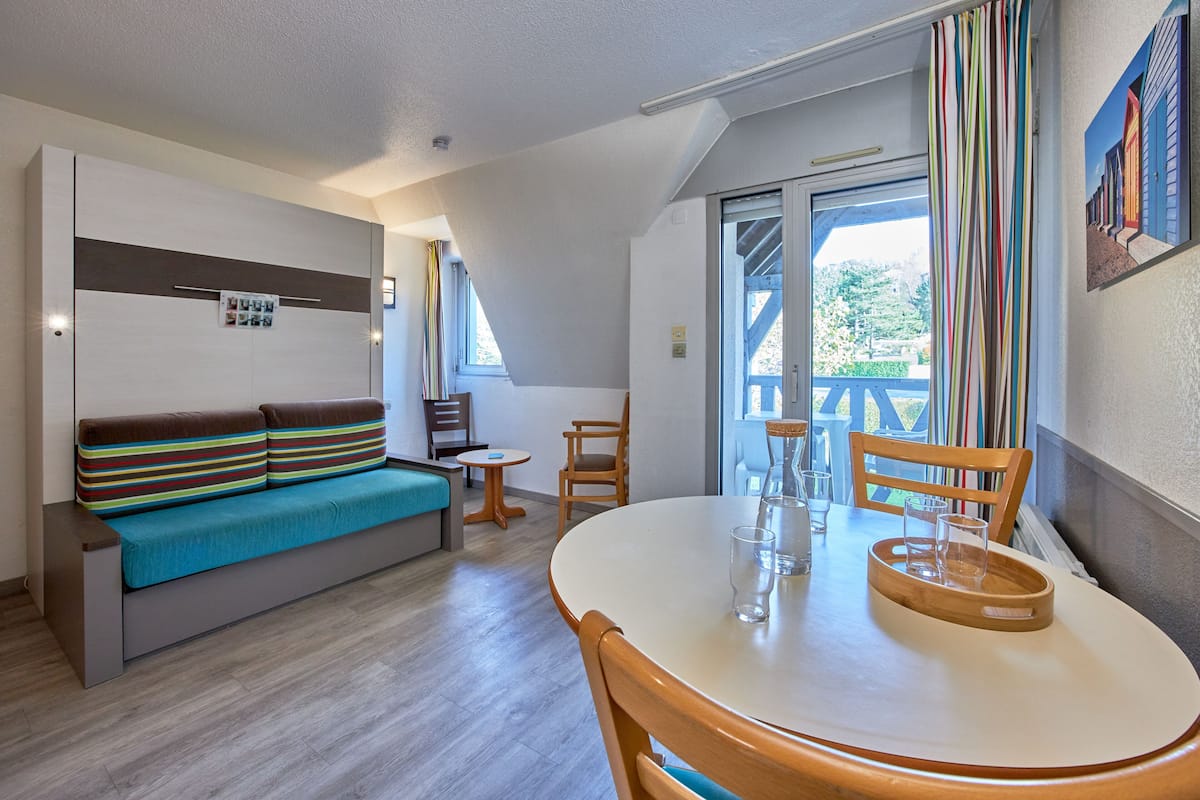 A compact living space with a sofa, a dining table, and a balcony with a view.