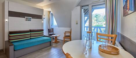 A compact living space with a sofa, a dining table, and a balcony with a view.