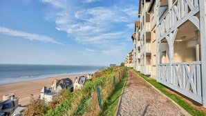 Un hotel frente al mar con vistas a la playa y al océano. El hotel presenta un diseño arquitectónico moderno con balcones y un camino de grava.