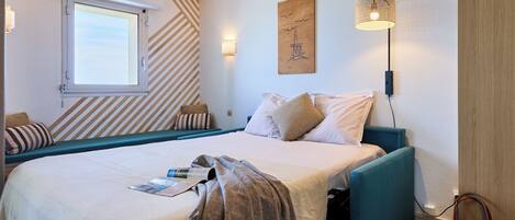 Un dormitorio con una cama, una ventana, una lámpara en la pared y un cuadro.